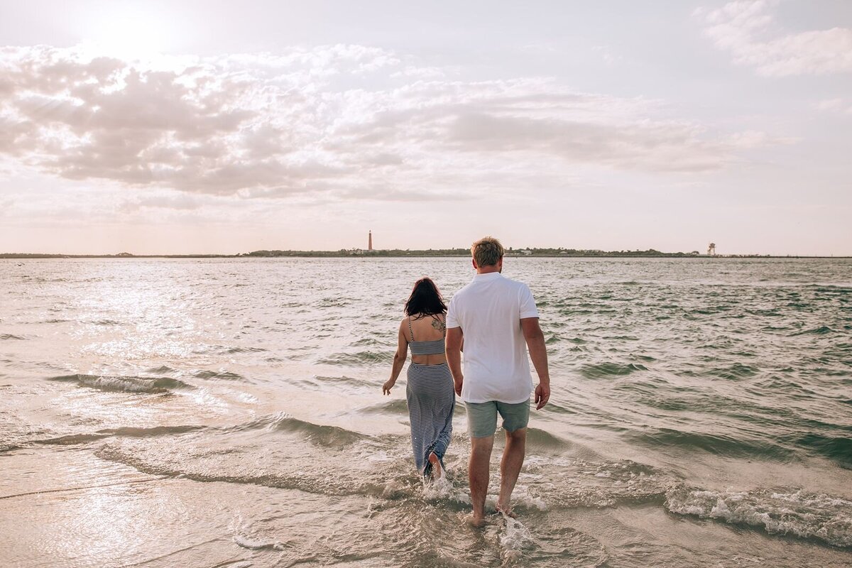 couple walking into the water at new smyrna with the ponce inlet lighthouse in the background