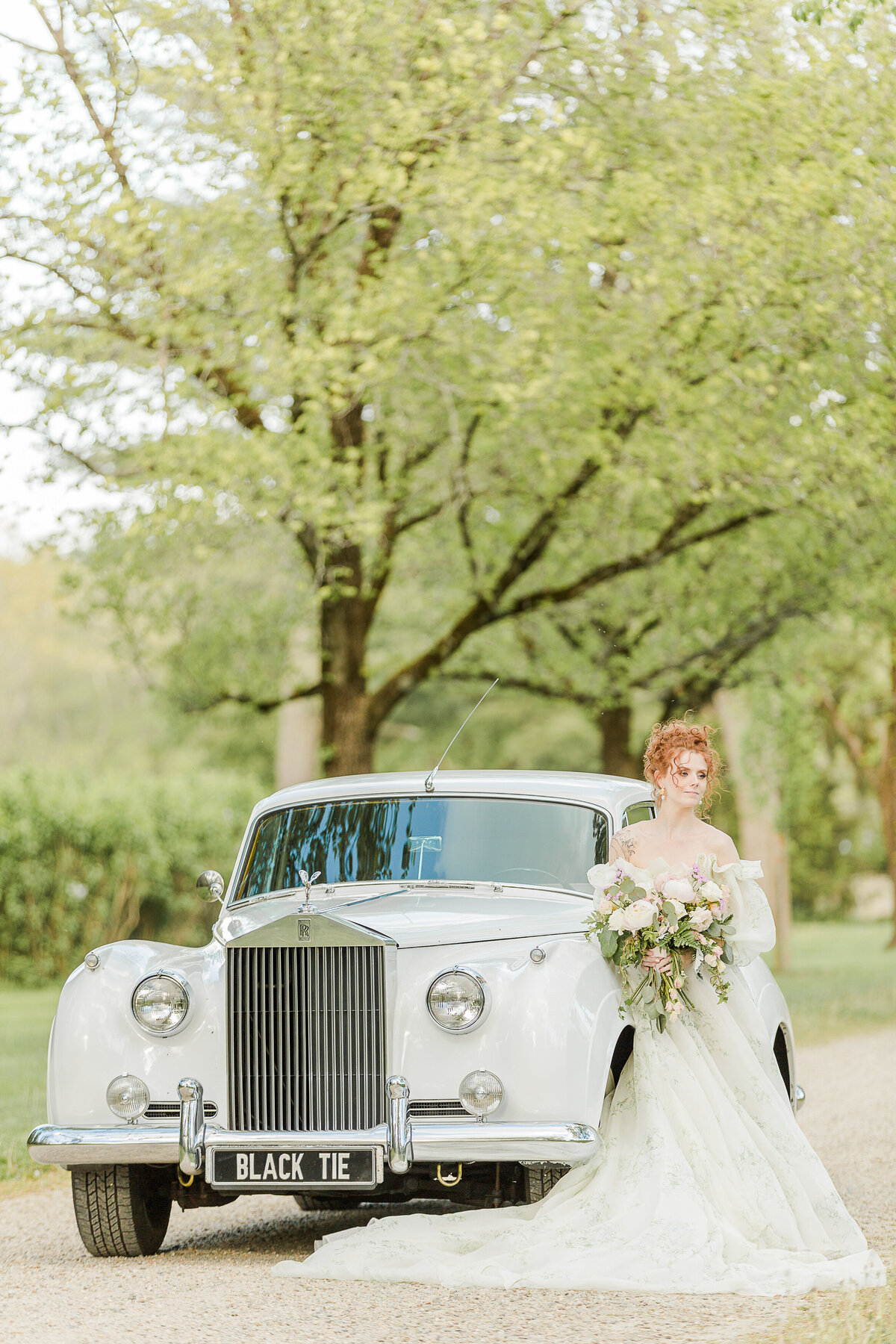 A bride stands in front of a vintage rolls royce for a stunning bridal portrait. She is holding her large blush bouquet in front of her and looking over her shoulder in the distance. Captured by Lia Rose Weddings, New England Wedding Photographer.