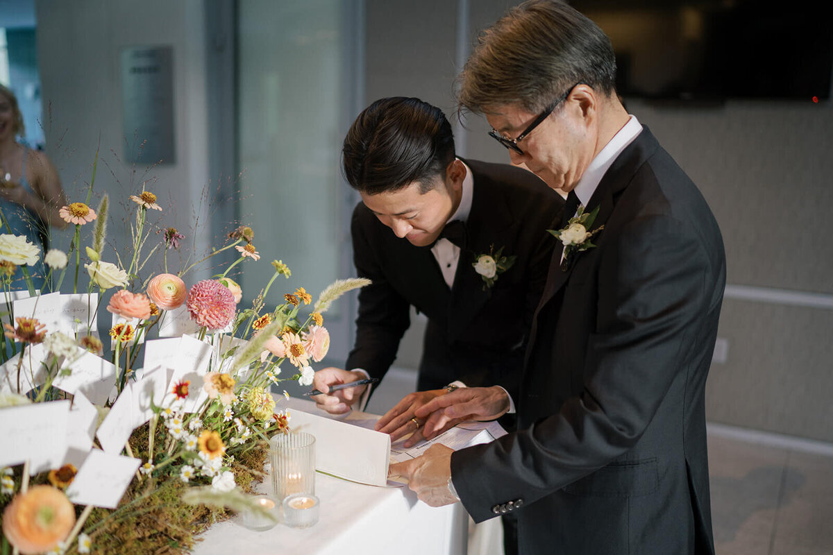 Groom at his Aspen Meadows Resort wedding reception venue signs the Colorado marriage license on a table featuring poppies and seasonal flowers.