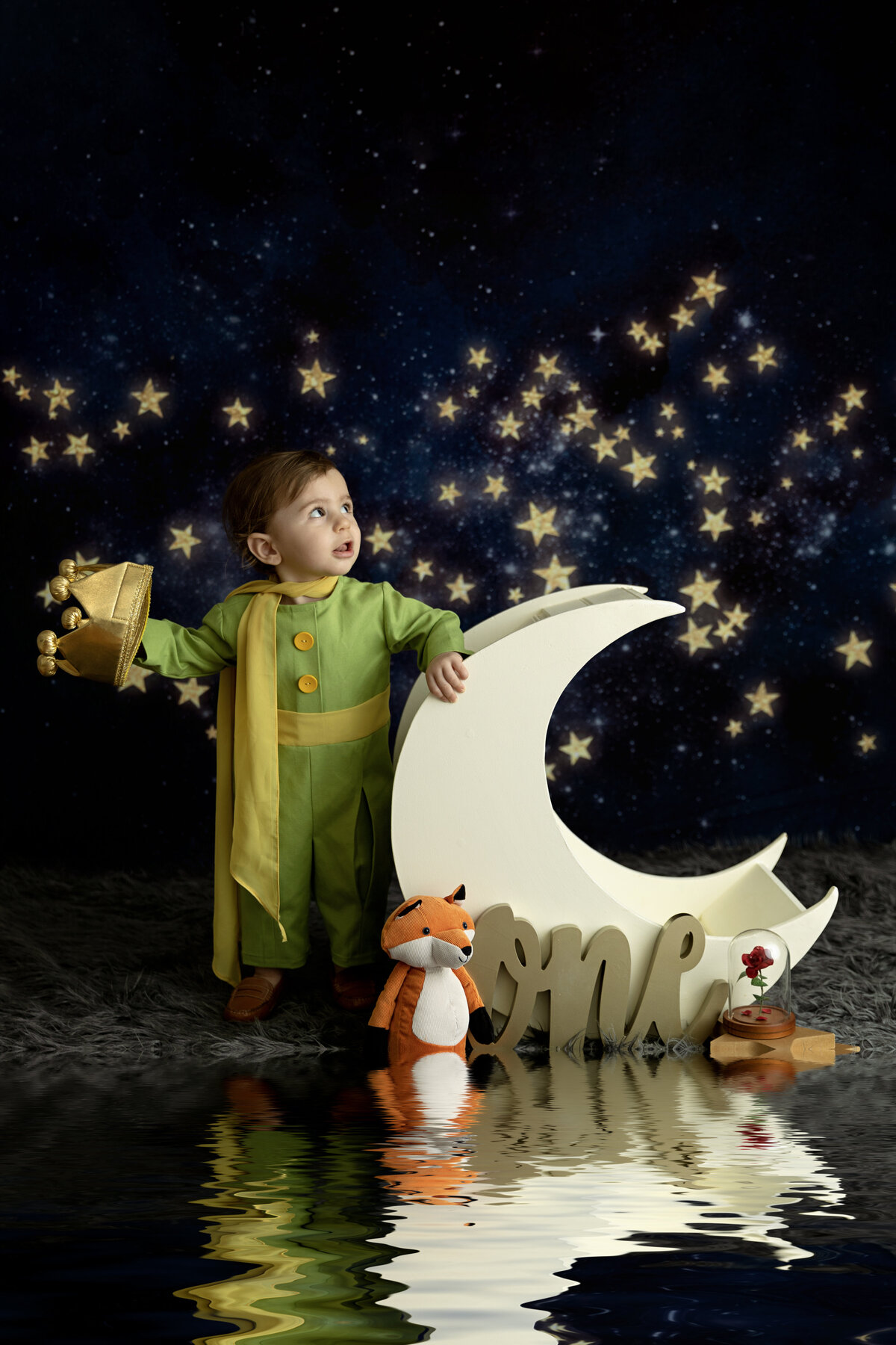 A toddler prince in a green outfit explores a moon shaped bed and a star background for his first birthday