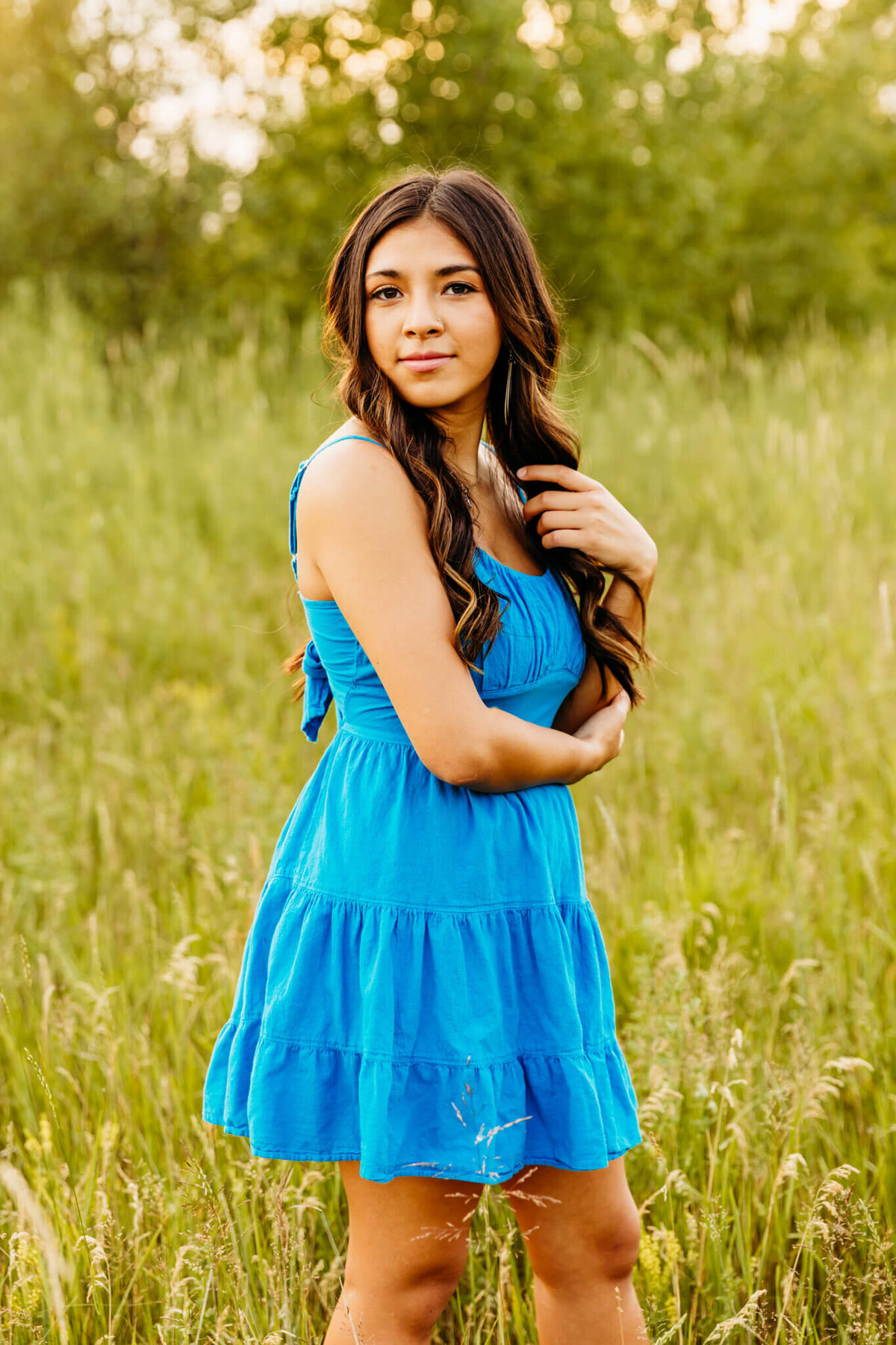 stunning senior in a blue dress playing with her hair in a field near Oshkosh