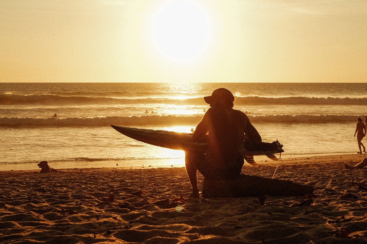 Man sitting with surfboard at sunset on the beach