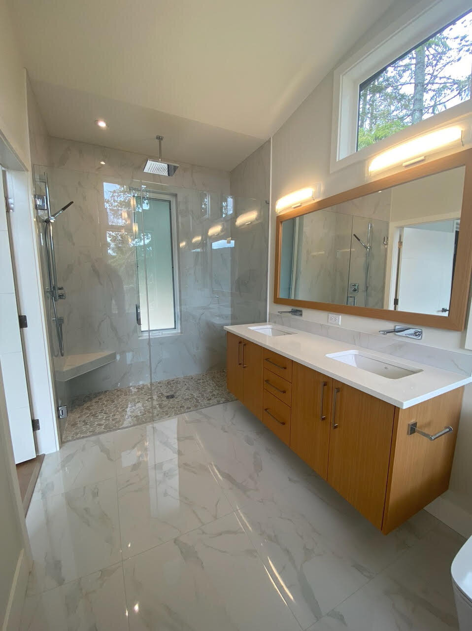 Bathroom interior design with walk in shower, pebble tile, rain shower, bench seat and double wood vanity with wall faucets