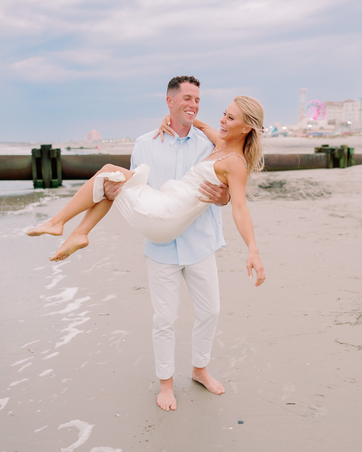 A person carrying their partner in their arms along a beach 