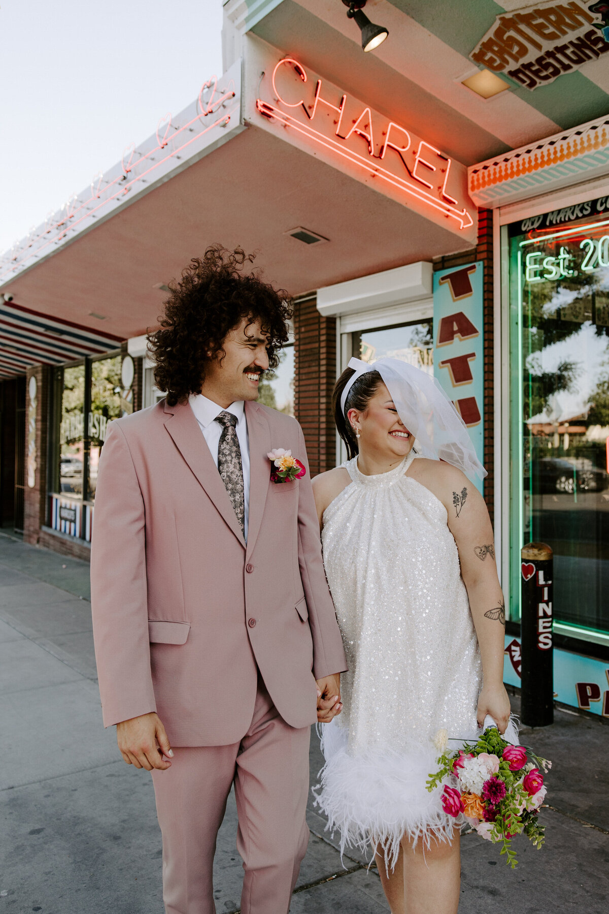 Two people on their elopement day smile in front of a tattoo shop.