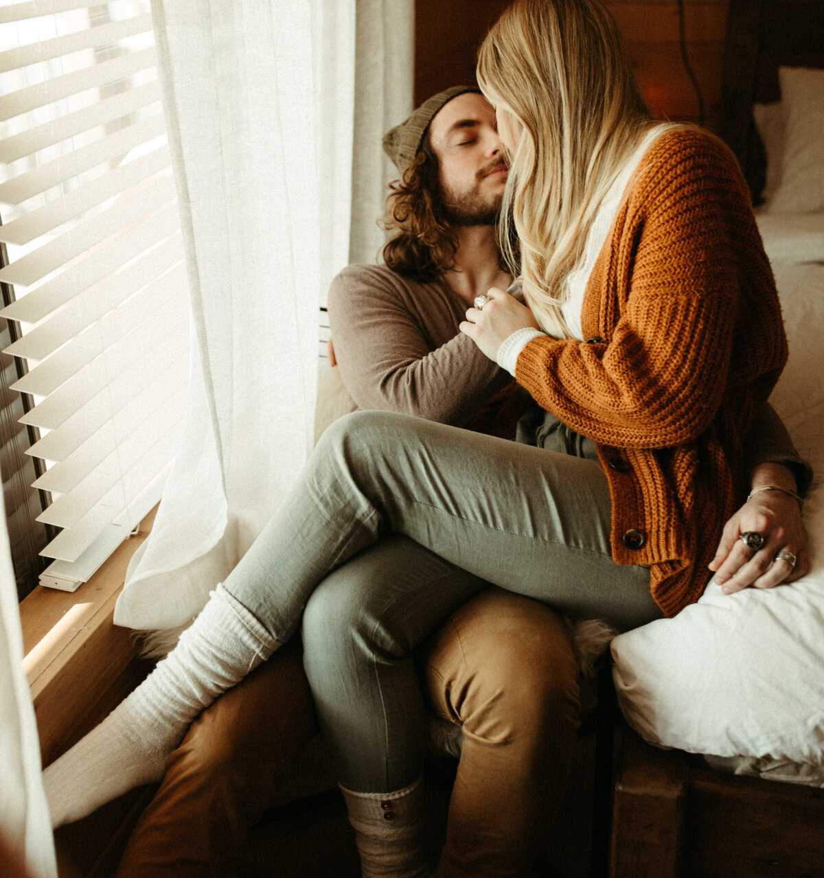 Couple in cozy winter outfit snuggling in their home next to a window