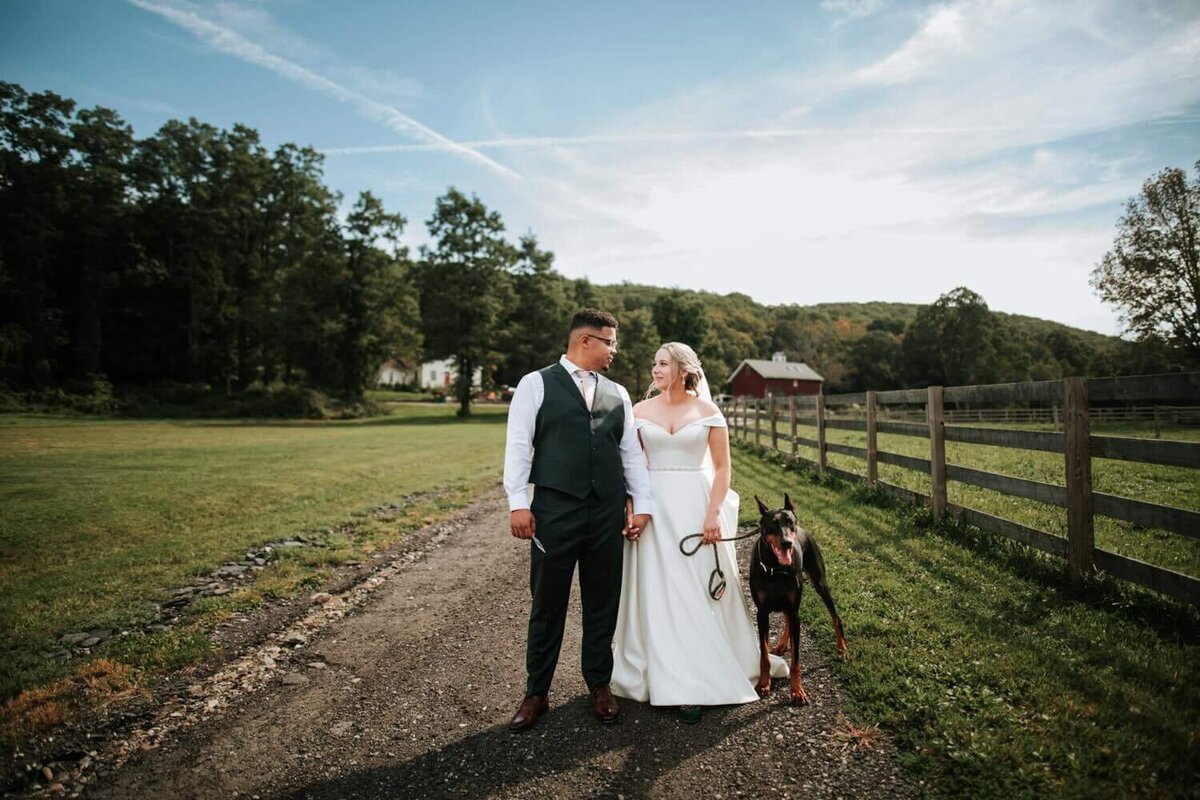 Bride and groom standing on a dirt trail with dog in Holmes New York sharing a special moment of isolation.