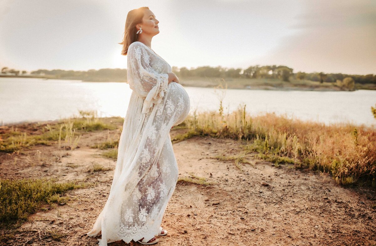 Pregnant woman with her eyes closed standing by the water with the sun shining on her face