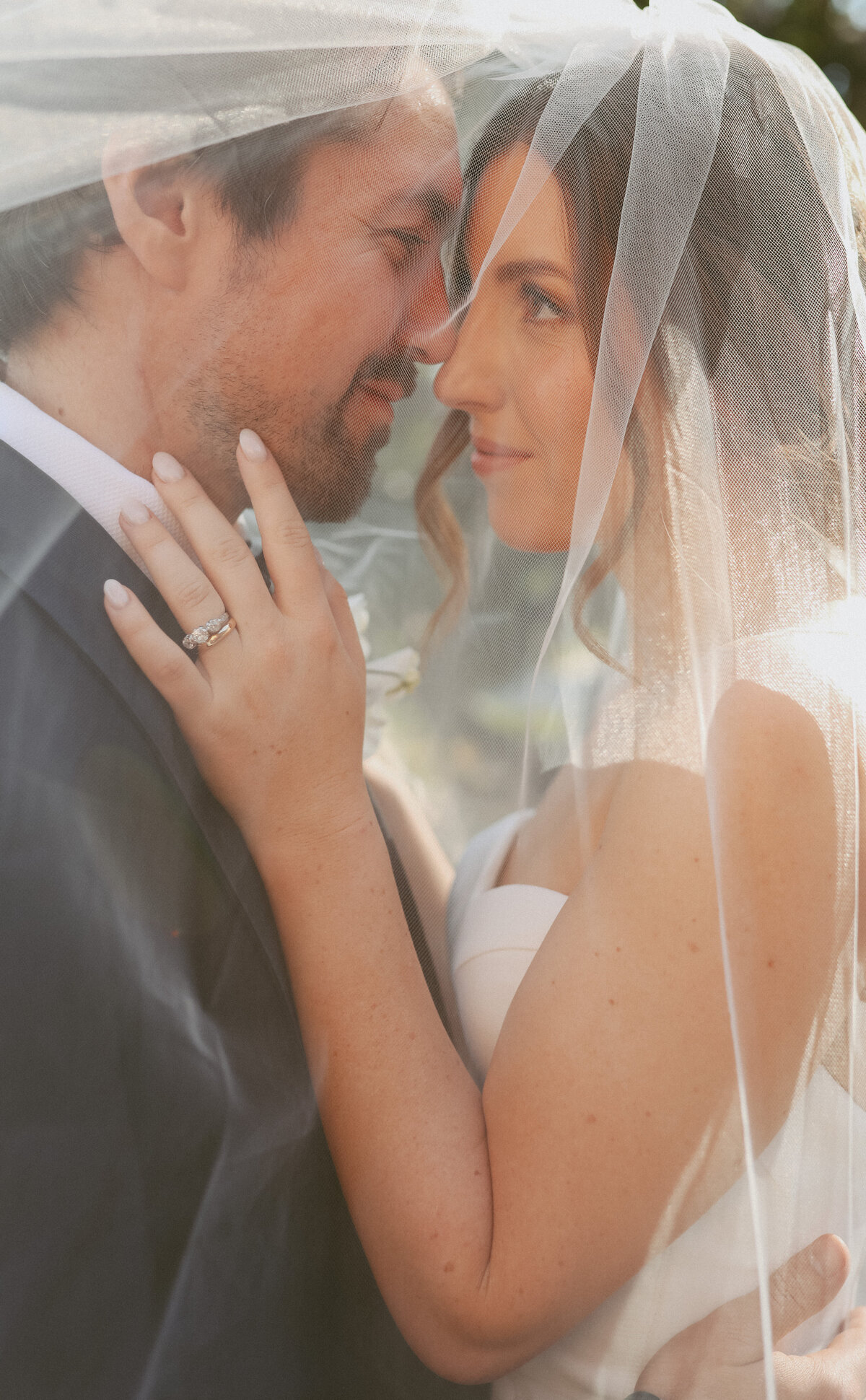 bride and groom under vail looking at each other