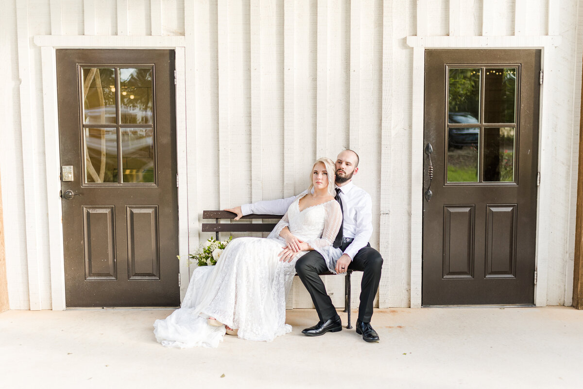 Bride and groom sitting outside white barn wedding venue in north Georgia