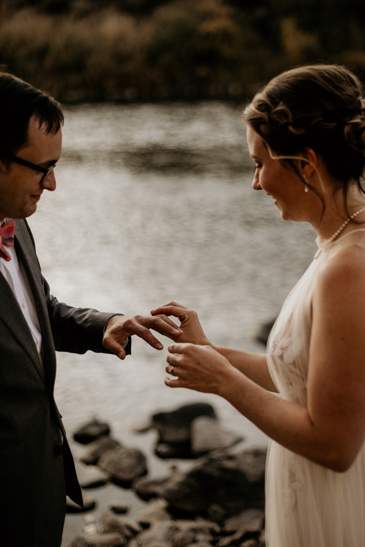 bride placing ring on grooms finger by a river