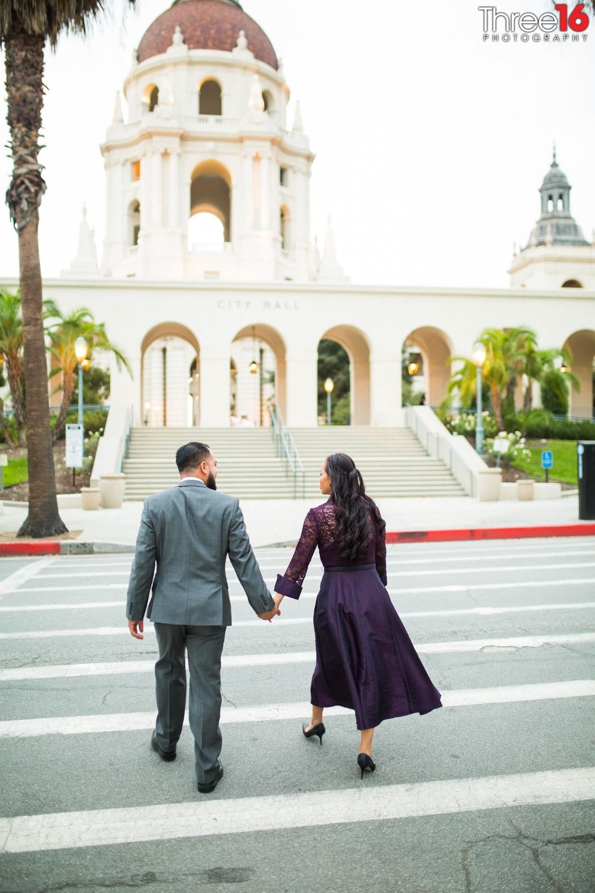 Engaged couple cross the street holding hands walking towards the Pasadena City Hall