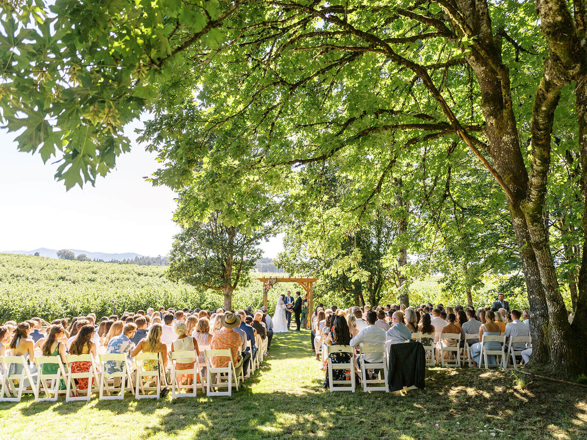 People seated at an outdoor wedding ceremony facing away from the camera.