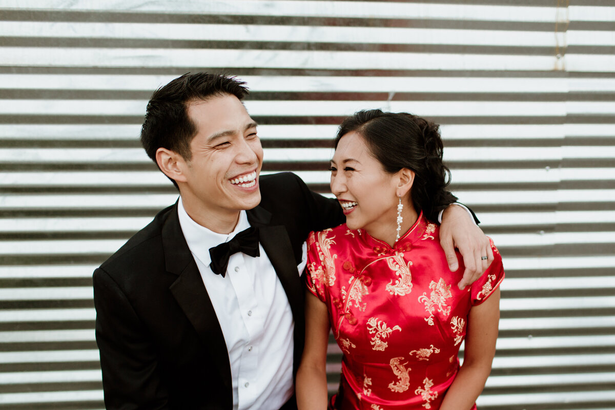 A bride wearing a traditional red chinese dress and her groom laugh in a candid moment captured by Fort Worth Wedding Photographer, Megan Christine Studio
