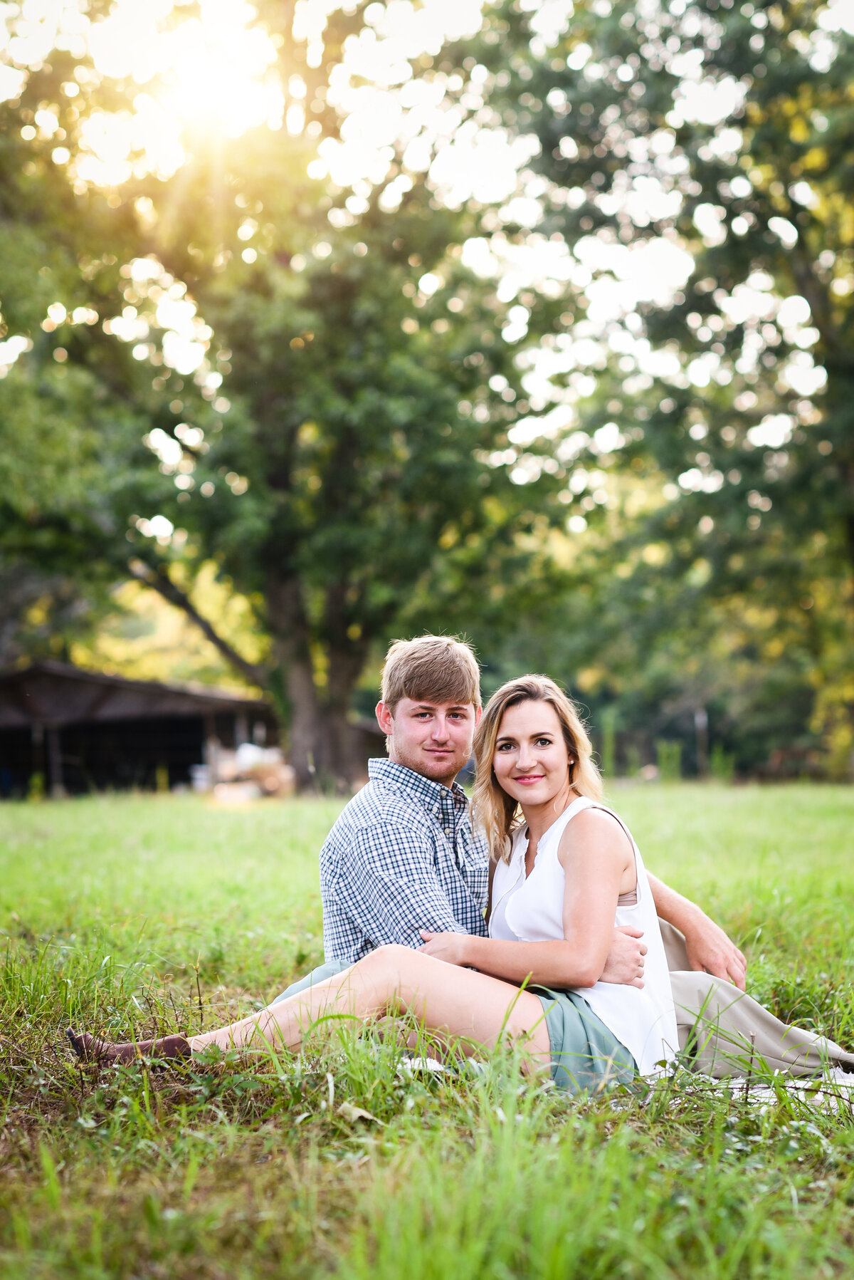 Beautiful Mississippi Engagement Photography: couple sits in a field during golden hour with sunset behind them