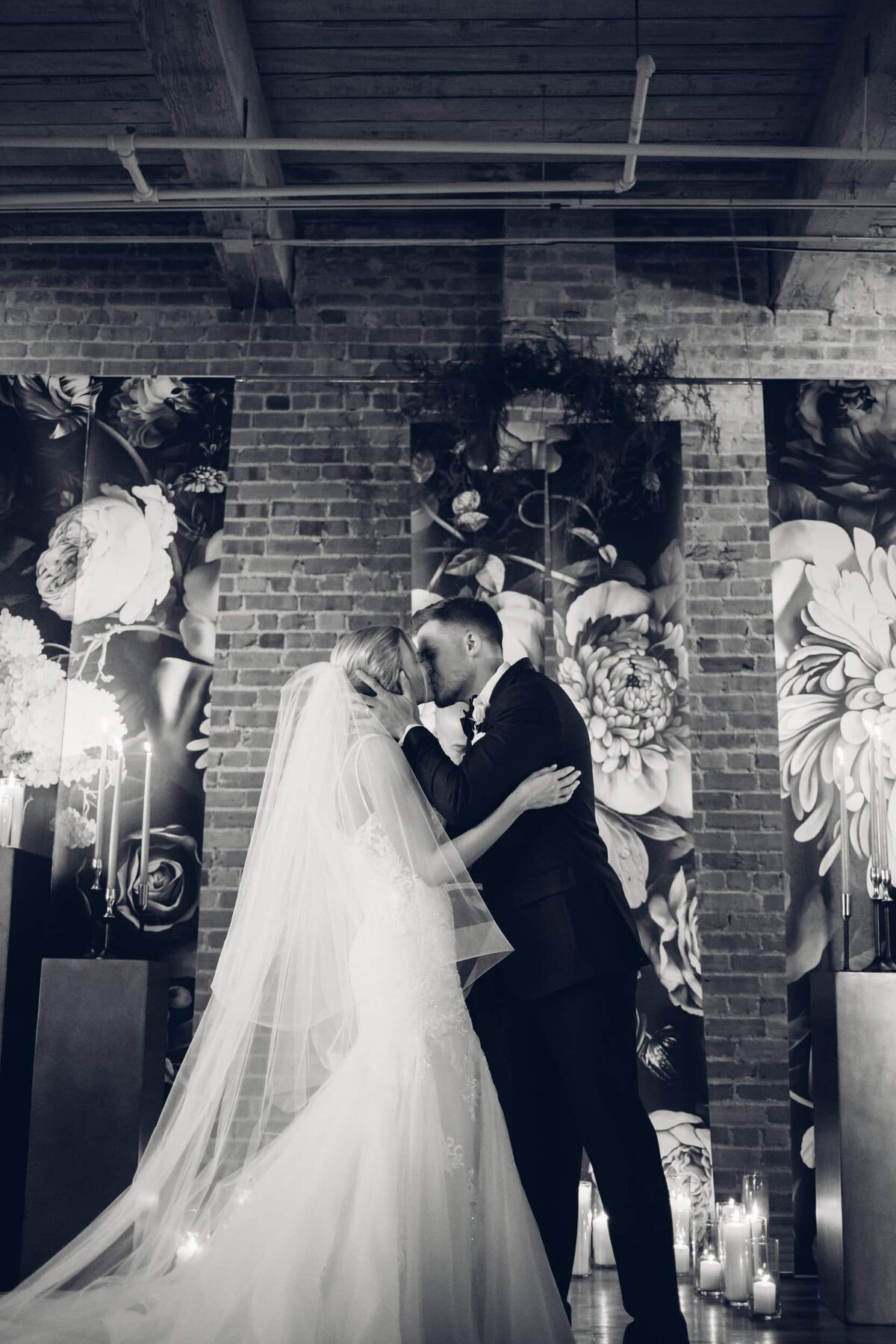 A bride and groom share a kiss in front of a stunning floral wall, captured by destination wedding photographer Britt Elizabeth.