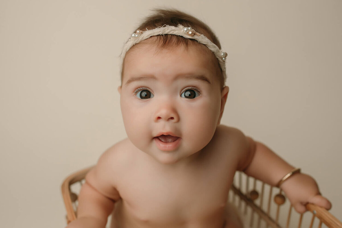 a six month old girl wearing a headband sitting in a wooden basket