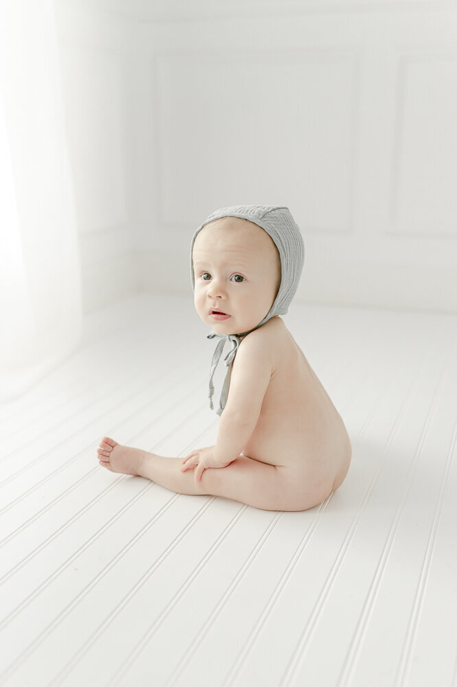 A 9 month old baby boy sits naked in a blue bonnet in kristie lloyd's nashville photography studio