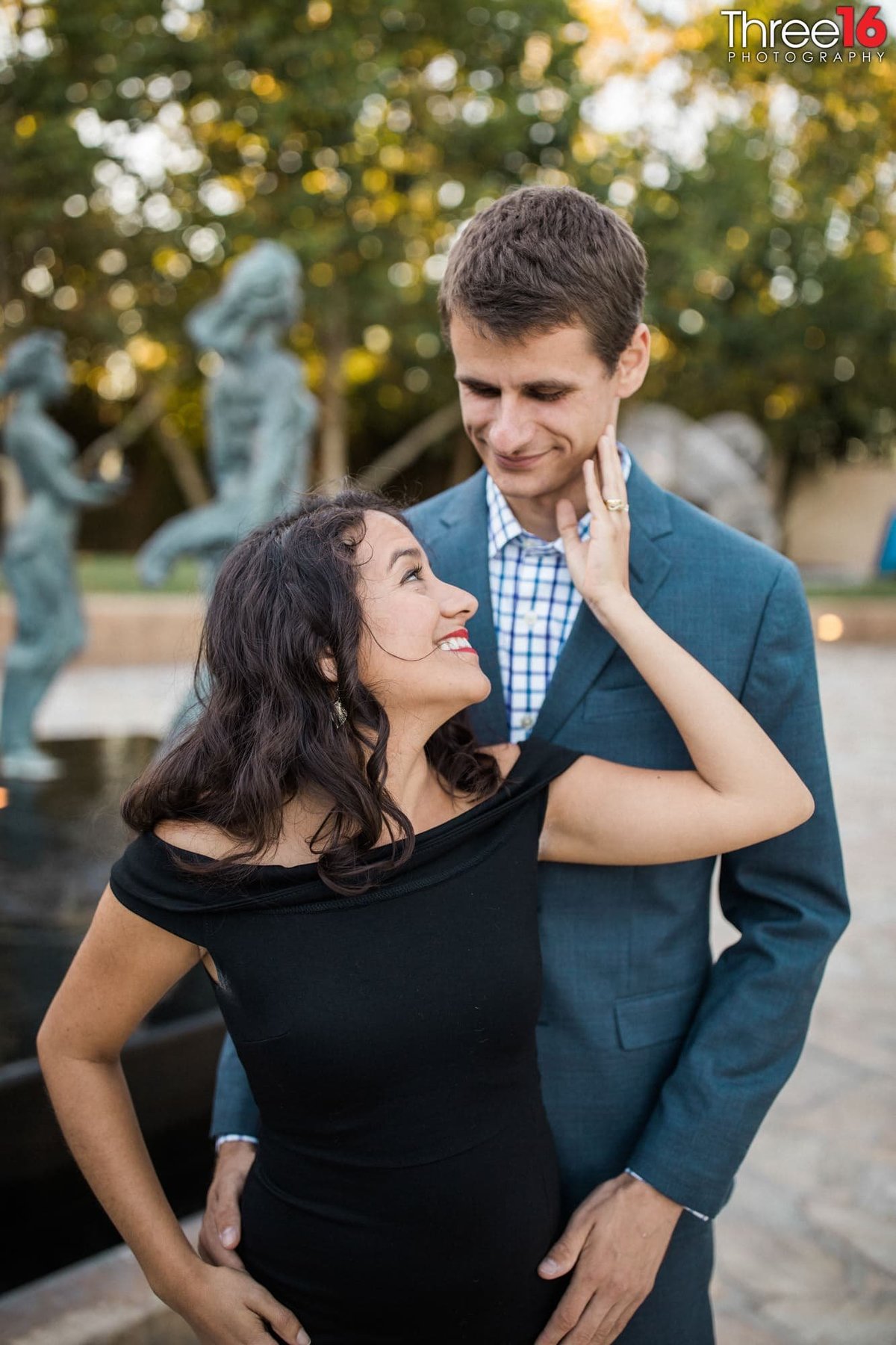 Groom to be holds his Bride's hips from behind as she looks up at him and smiles during an engagement photo shoot