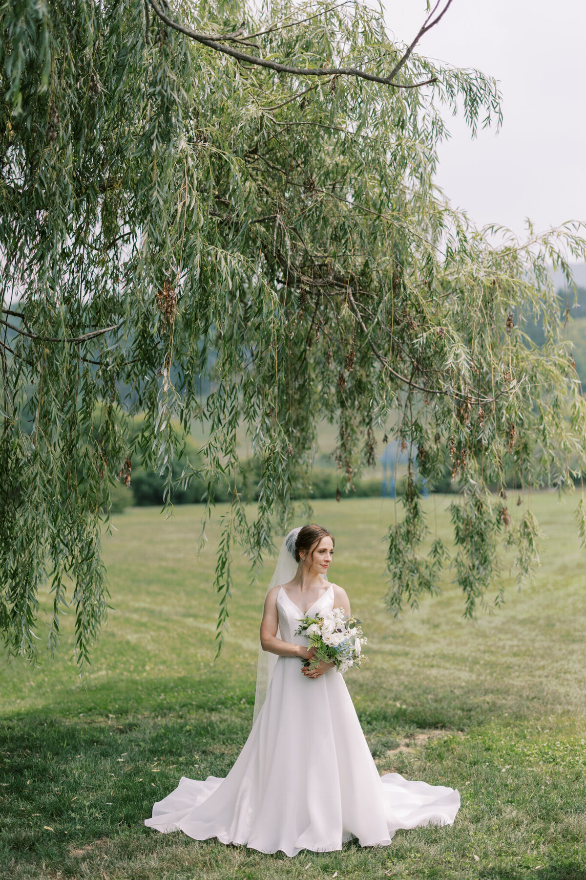 Bride stands under willow tree in elegant ceremony