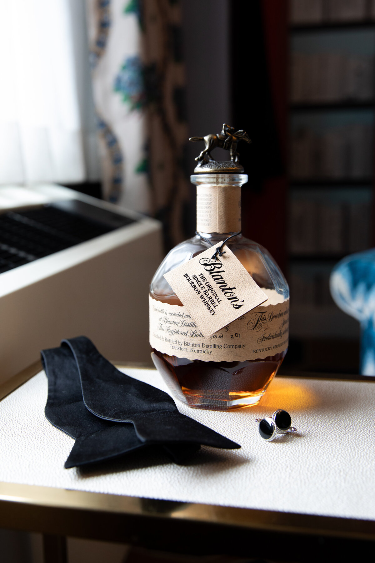 Rhode Island Wedding Photographers | Kelsey Sheehan Photography Timeless Rhode Island Weddings | A bottle of Blanton's bourbon with a horse-shaped stopper is set beside a black bow tie and cufflinks on a white surface, evoking elegance and sophistication.