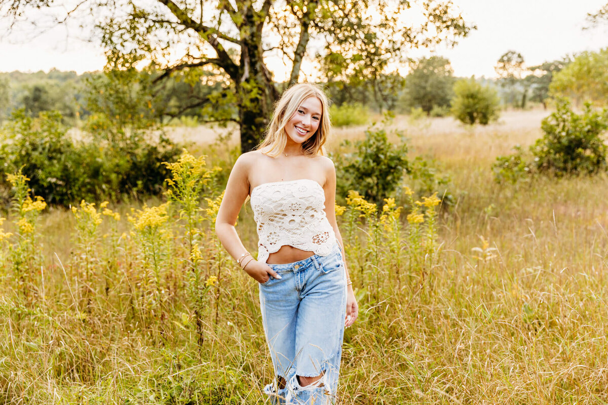 gorgeous blonde teen girl in a lace top and jeans walking through a wildflower field at sunset near Appleton. 