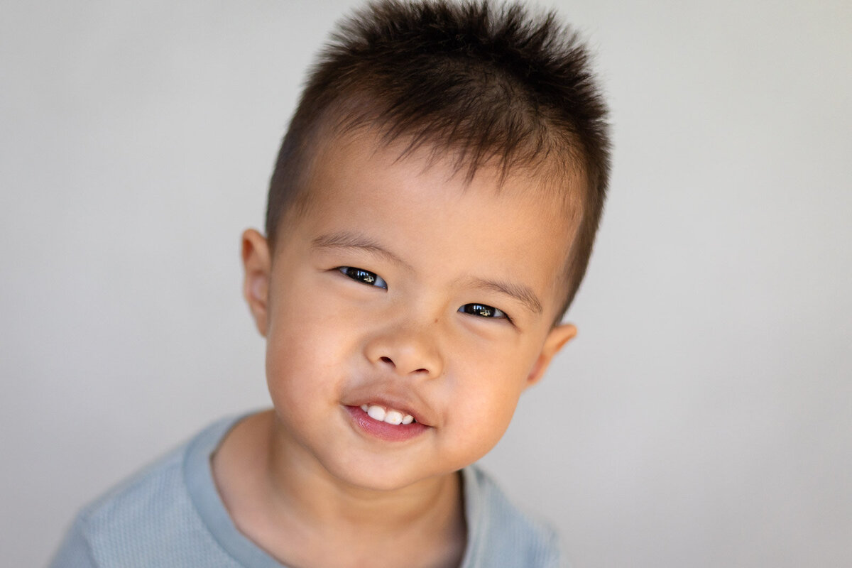 Toddler smiling in blue shirt against a light background during Bay Area School Photography at a local preschool – Ellobelle Photography