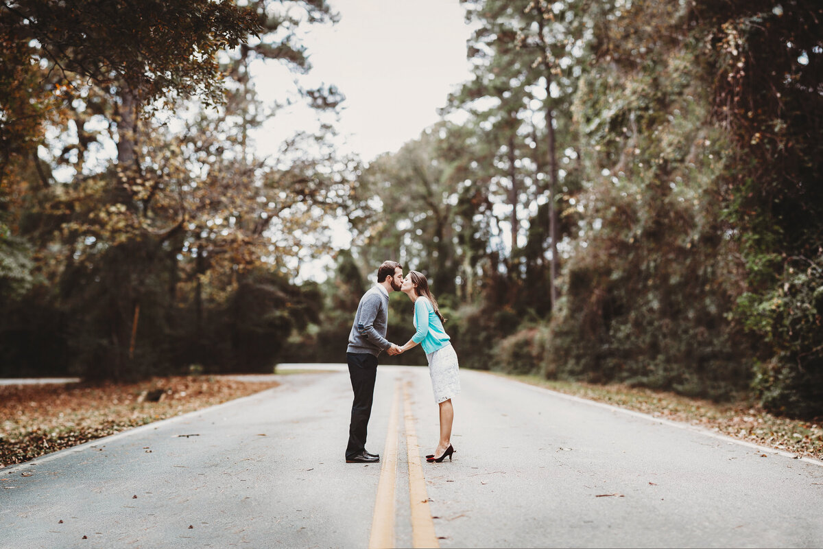 Couple sharing a kiss on an empty forest road during a fall engagement session in Winter Garden, Florida.