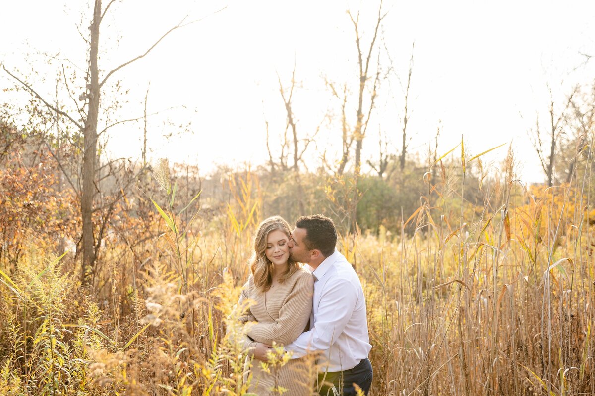 Guys-kisses-his-fiance's-cheek-as-he-embraces-her-tightly-from-behind-at-meadowlily-park-during-a-fall-engagement-session