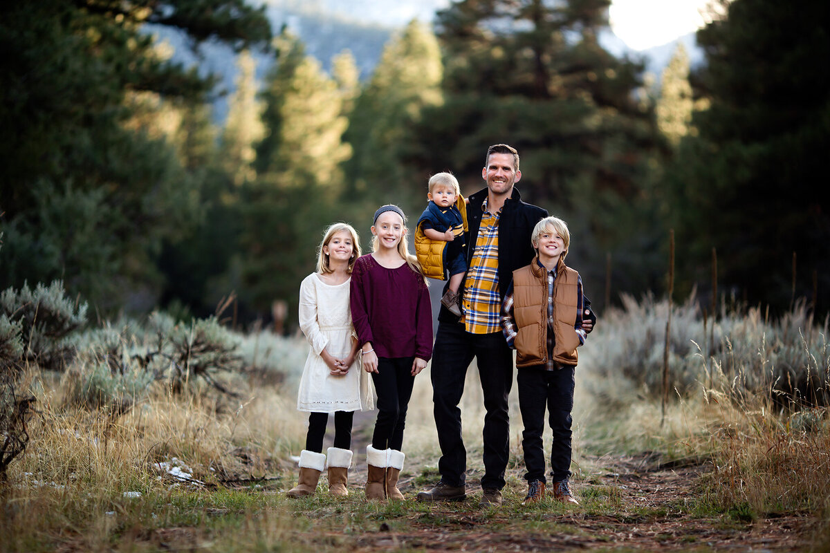 A family poses outdoors in a serene forest setting, captured by a Dallas family photographer. The parents and children stand together, showcasing a warm, joyful moment.
