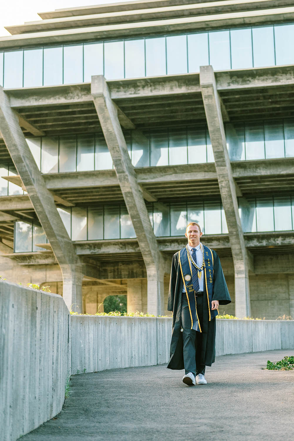 UCSD graduate wearing cap and gown walking away from Geisel Library