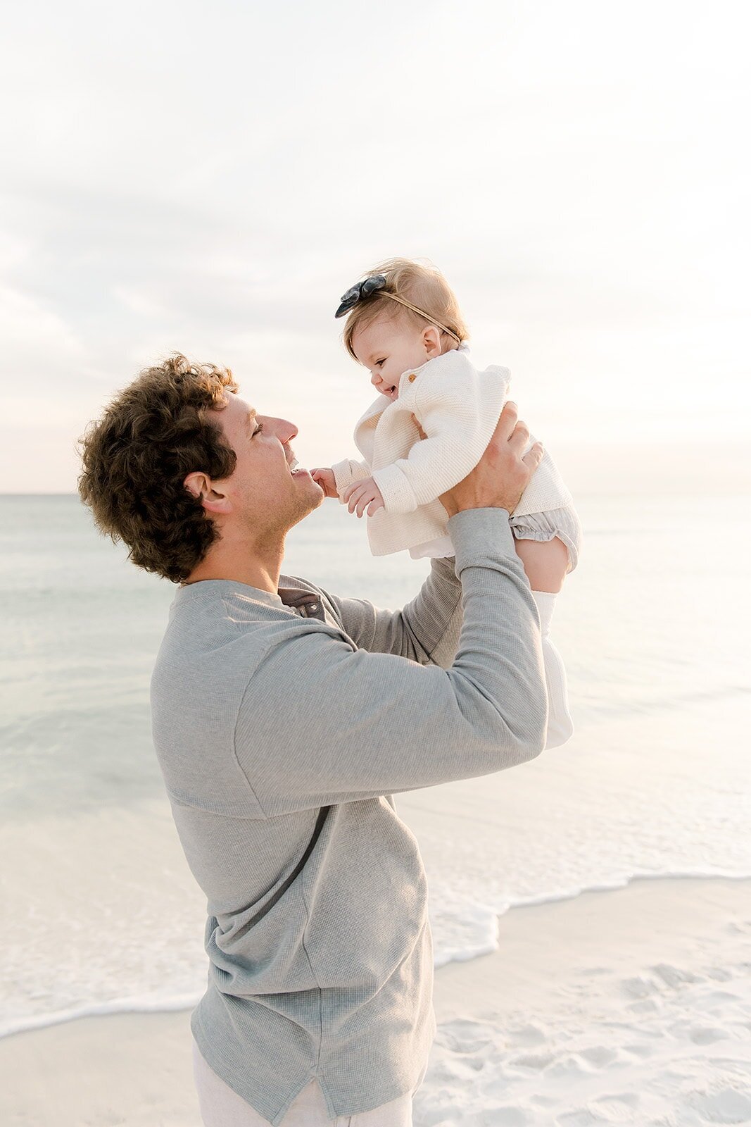 a dad holding his baby up in the air by a beautiful beach location in Destin during photography session