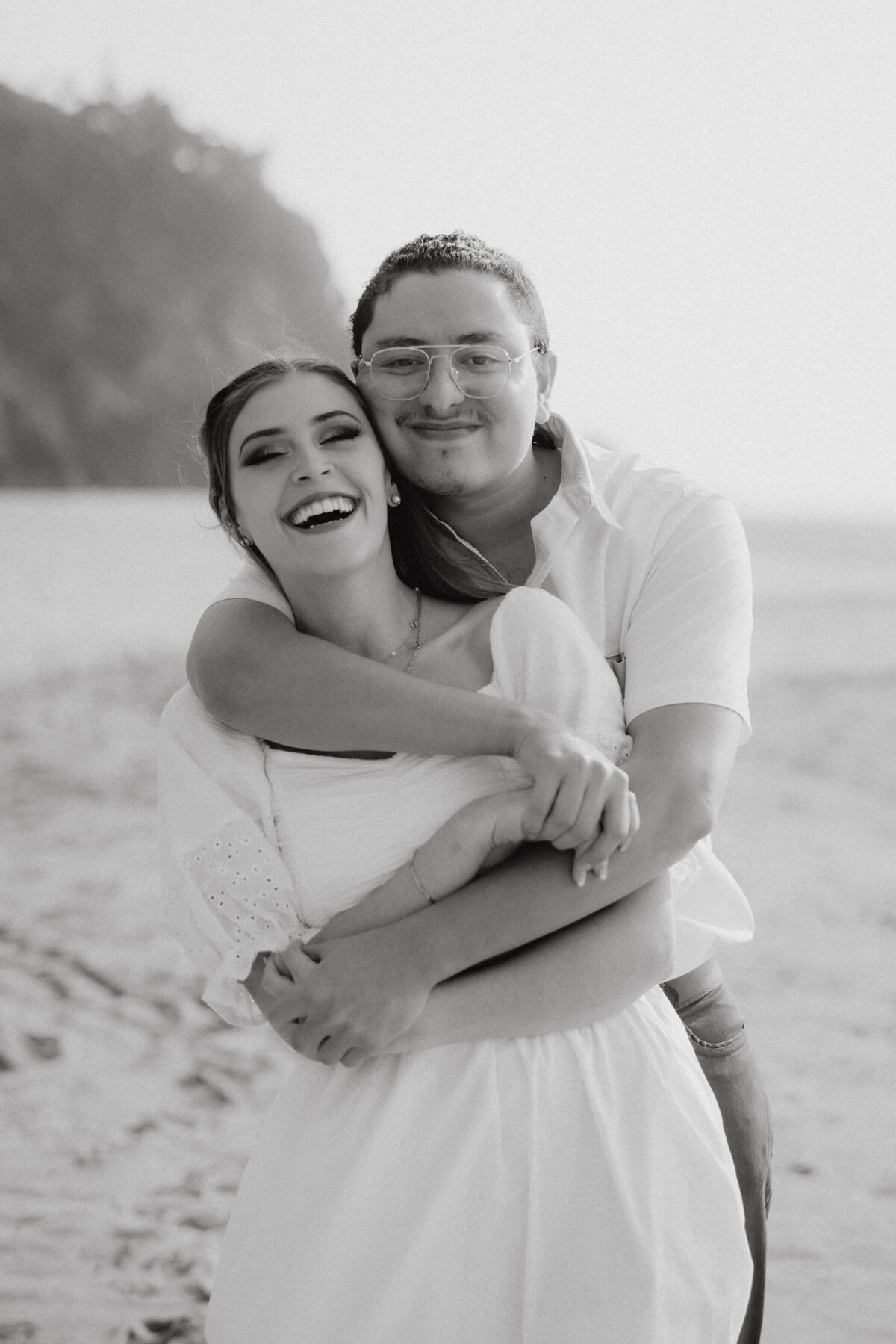 an engaged couple hugging on the beach