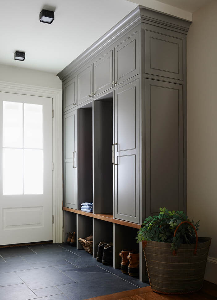 A classic mudroom design with slate flooring, grey cabinets, and a walnut bench. Designed by Sarah Scales in a historic Boston brownstone.