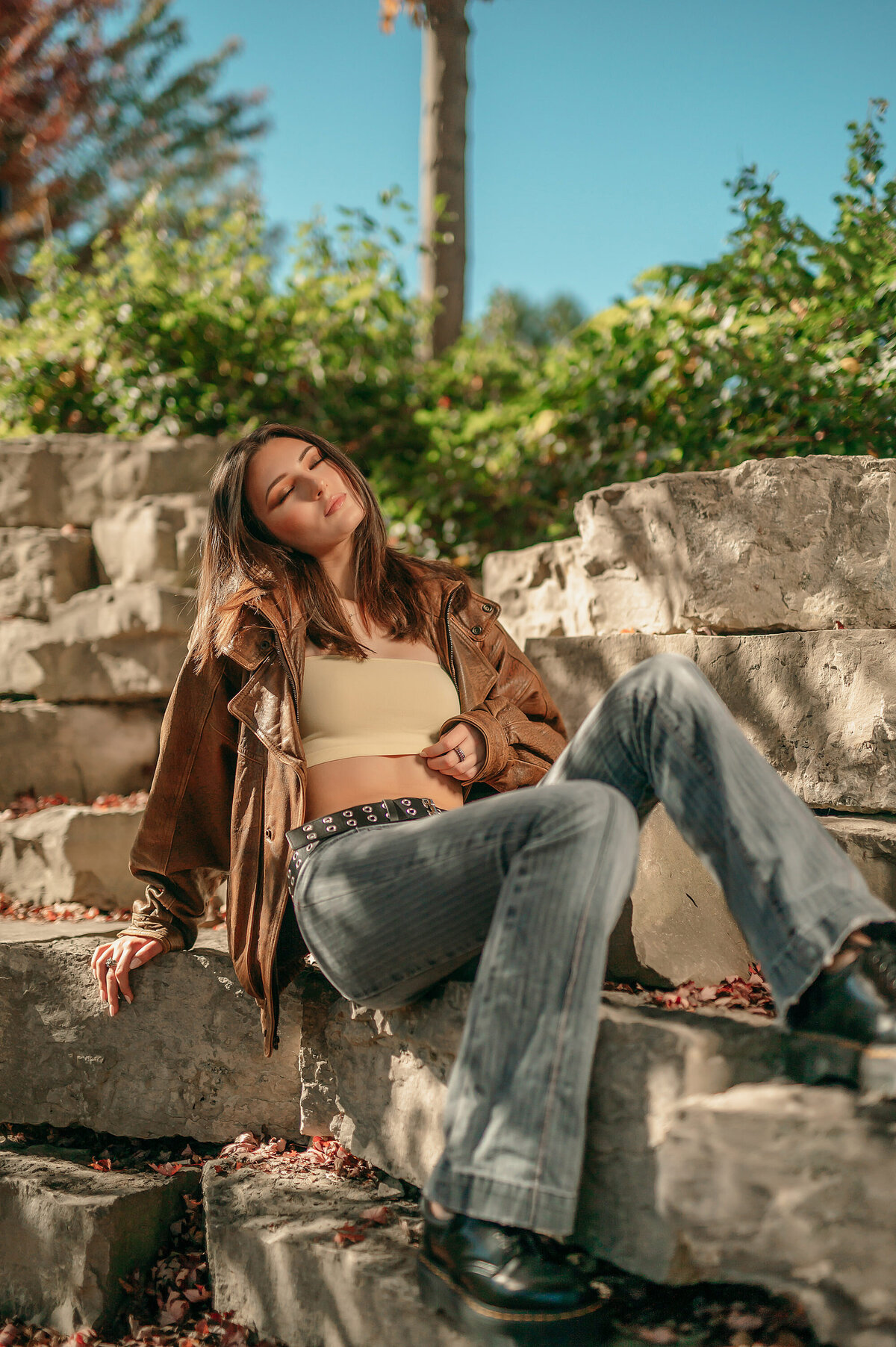 A Waukesha West High School senior sits reclined along a retaining wall in Minooka Park wearing jeans and a leather jacket..