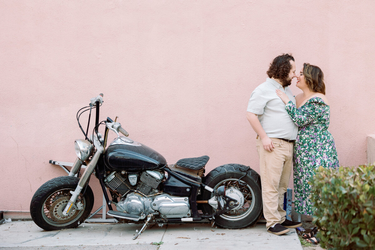 A couple about to kiss while standing next to a motorcycle