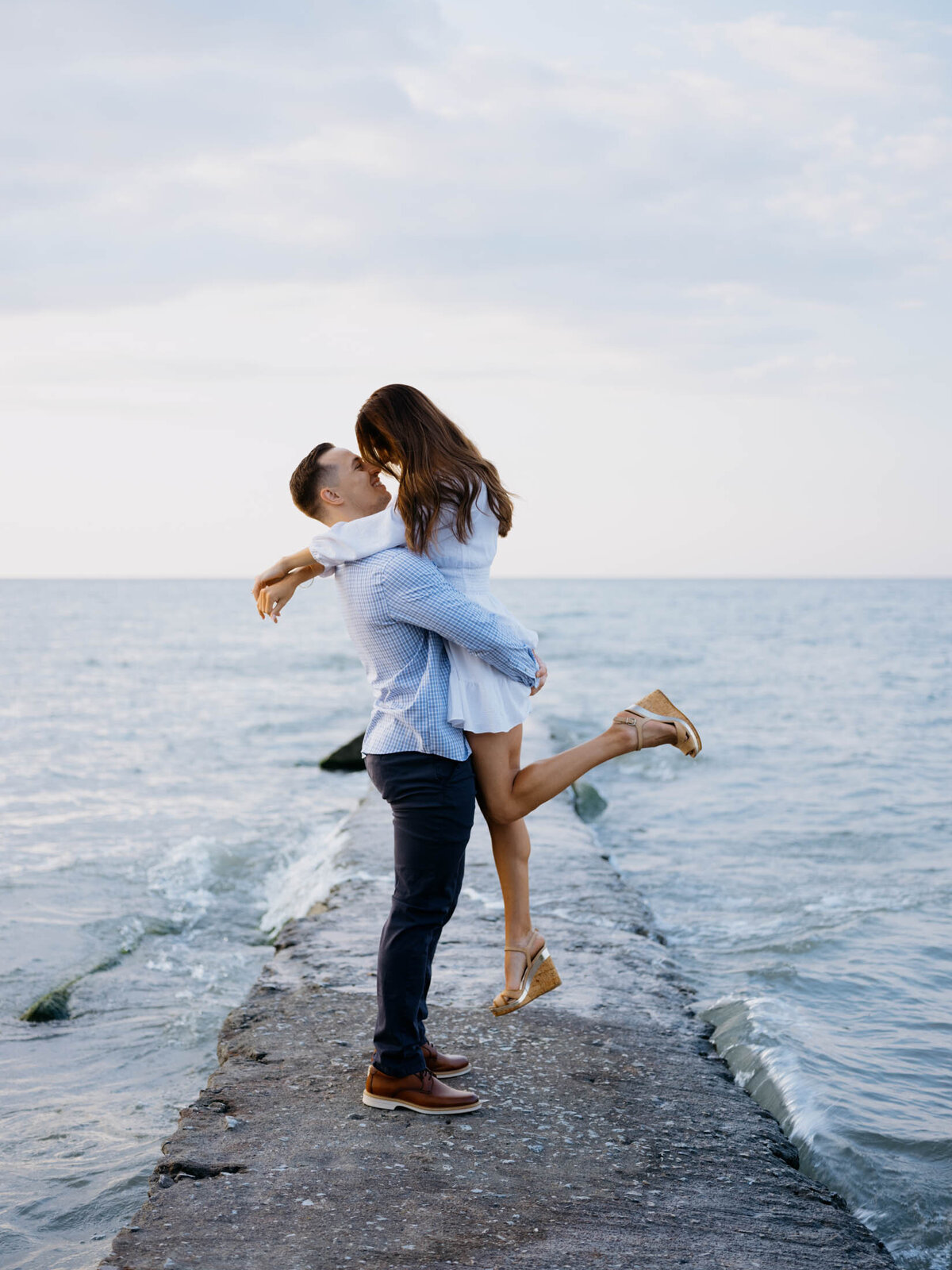 Groom picking bride up for a kiss at the beach during their engagement session.