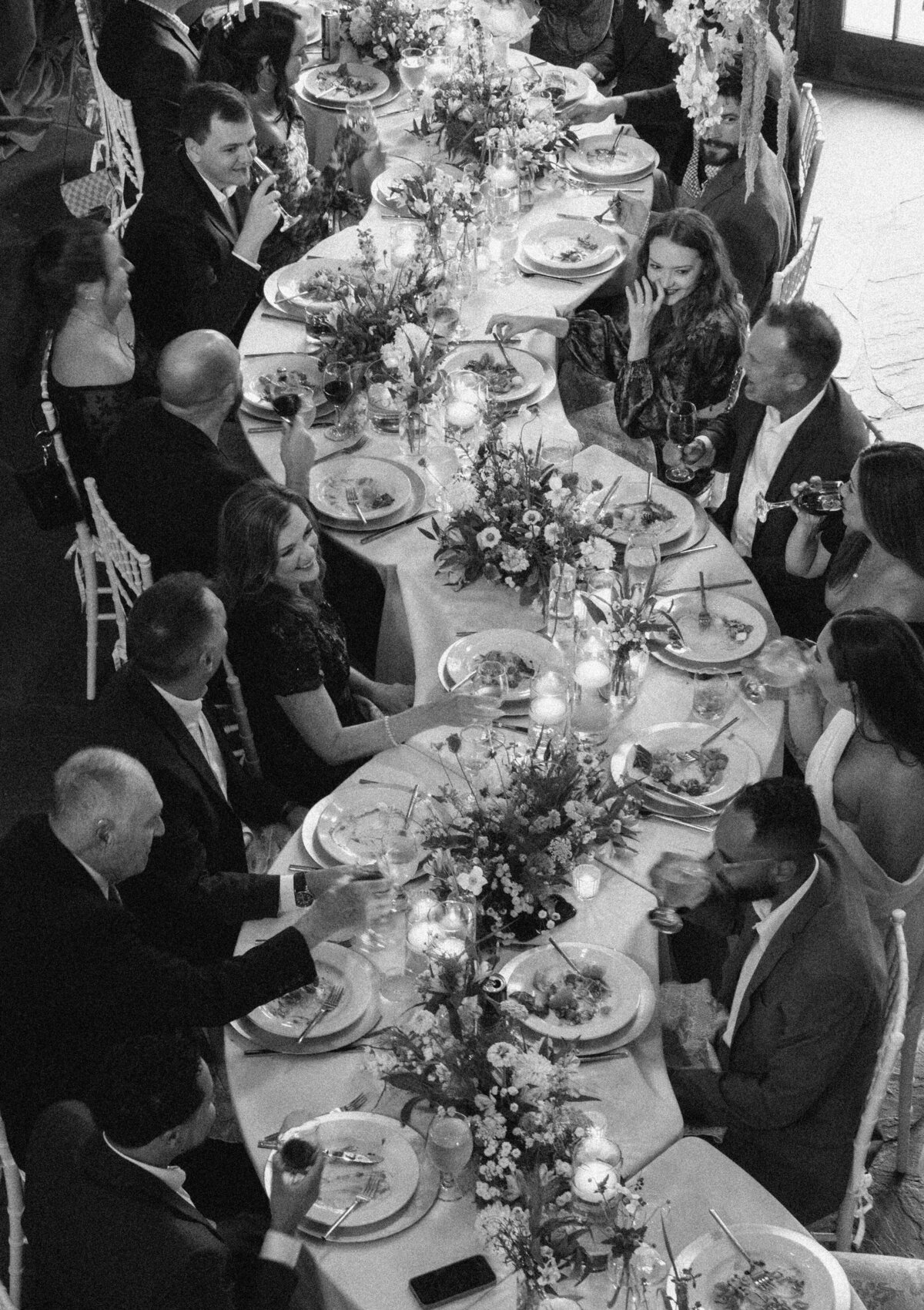 Black and white photo of wedding guests enjoying an intimate dinner reception at a long table at Castle Ladyhawke.