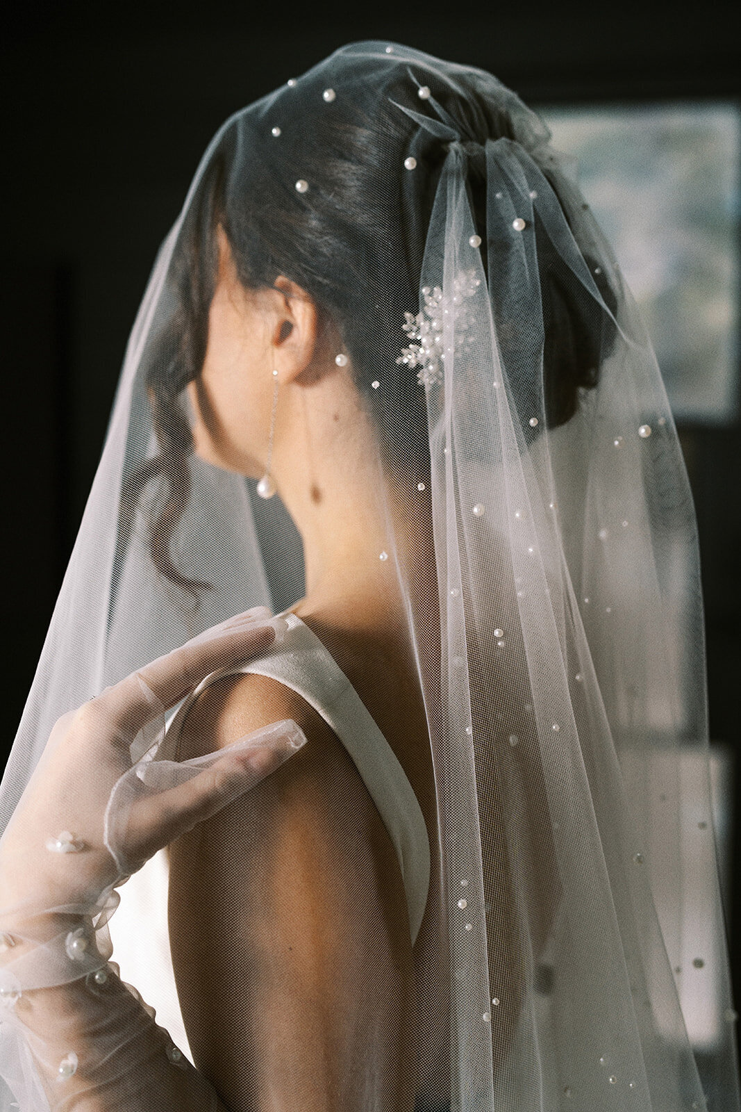 A bride wearing a veil and gloves. She is facing away from camera and has a hand on her shoulder.