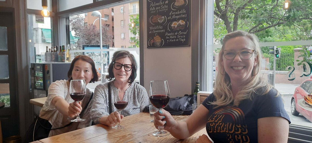 Maria Cristina and two women sitting at a table while holding their glasses of red wine and posing for a picture.