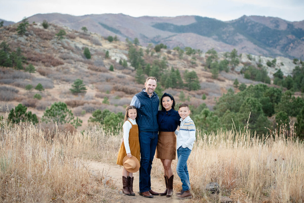 An image taken by a Denver family photographer of a family of 4 with arms around each other while standing in tall golden grass