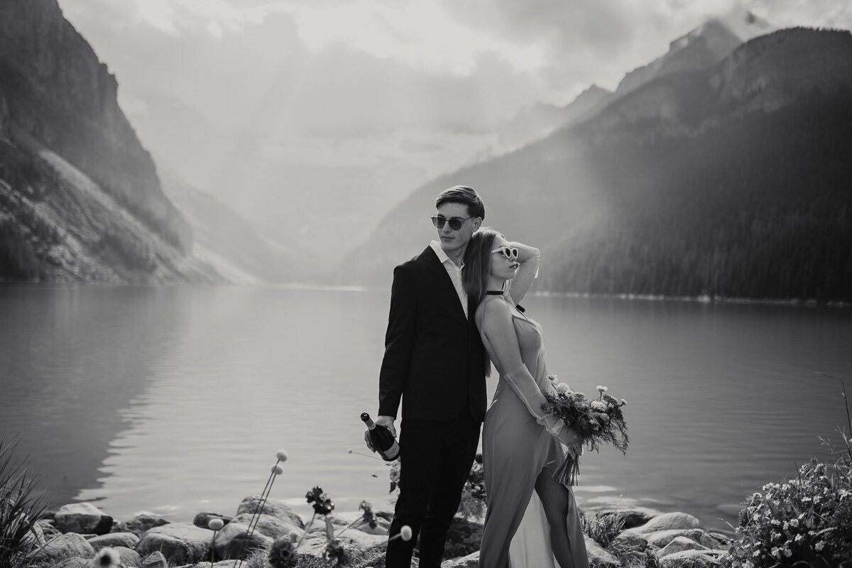 Couple in very trendy outfits infront of lake louise with a bottle of champagne