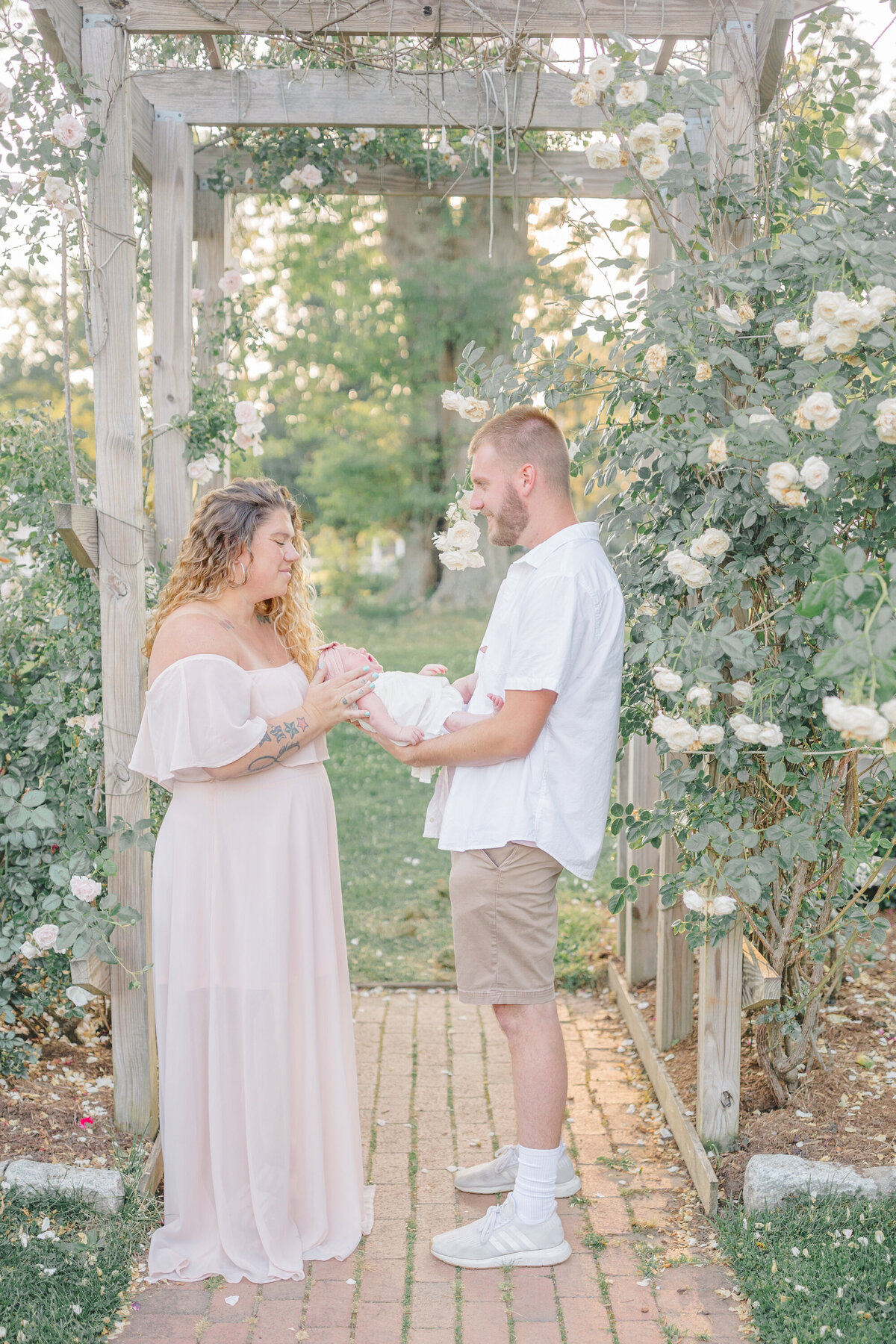 A tender newborn photo session featuring a loving mom and dad holding their precious baby in a beautiful English garden. Surrounded by lush greenery and delicate blooms, the parents gaze adoringly at their newborn, capturing the essence of love and new beginnings. Photographed by Oak & Lore Studio, this session blends timeless elegance with heartfelt connection