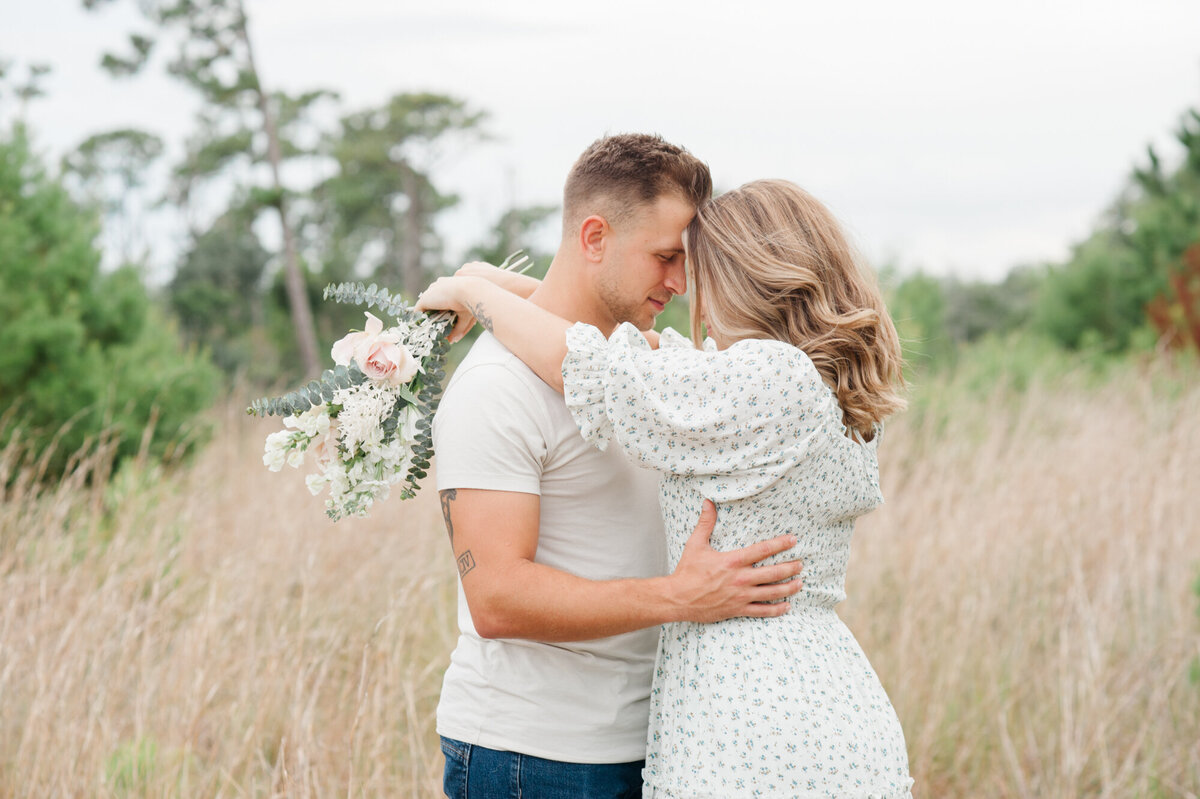 Wife holding a bouquet of flowers while hugging her husband in a tall grass field