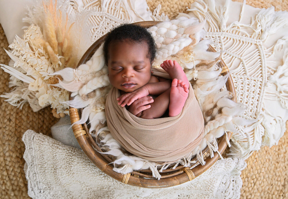 newborn baby boy wrapped in beige in a bowl on a boho style background for his newborn photos in Burlington, Ontario.