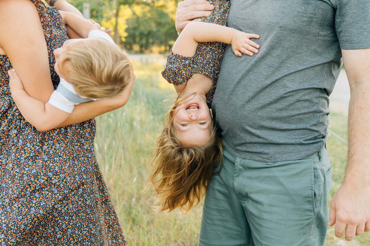 dad holds smiling little girl upside down
