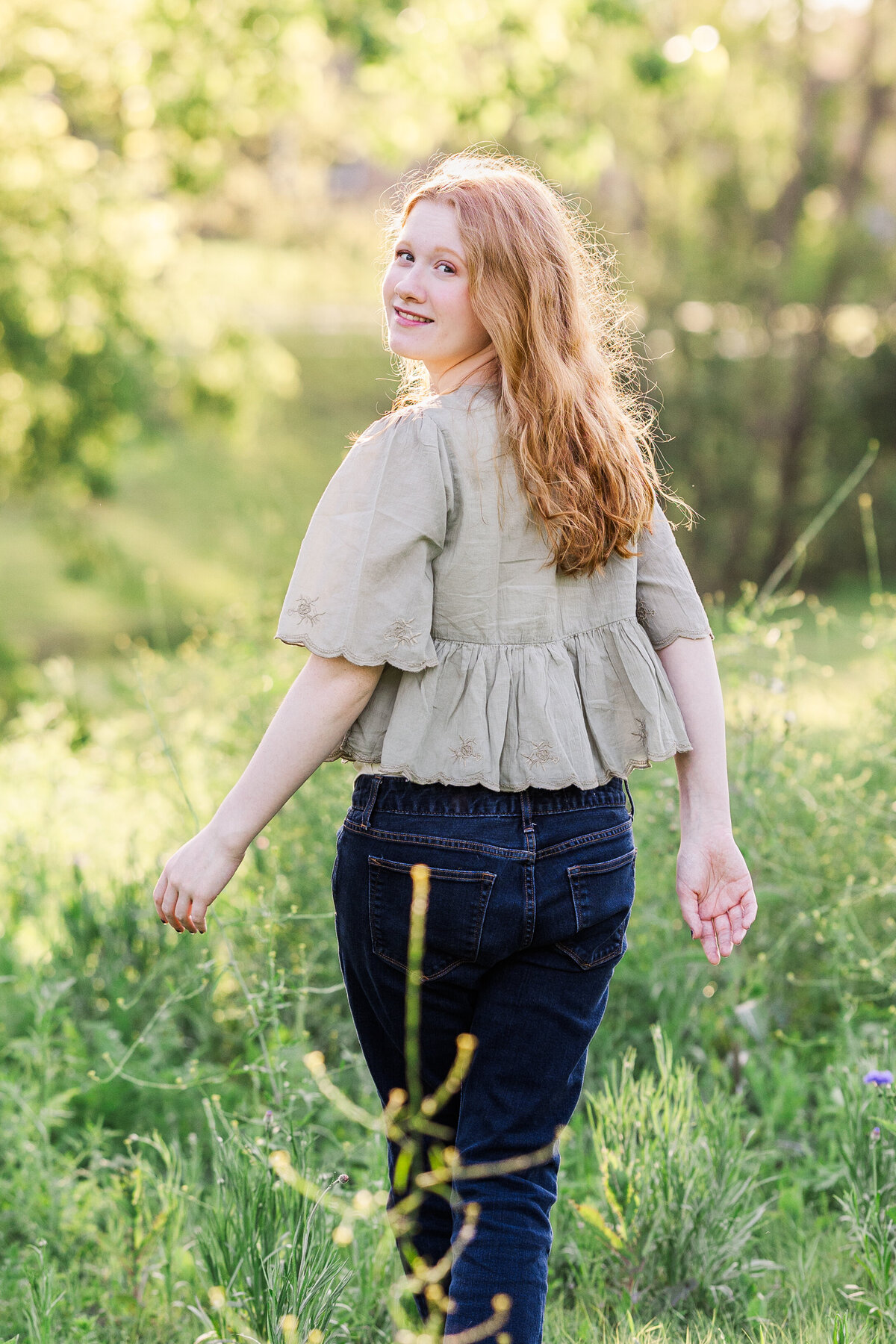 A joyful senior session captured in a sunlit field in Plano, Texas. Natural golden light highlights her soft smile and red hair for a warm, whimsical look.