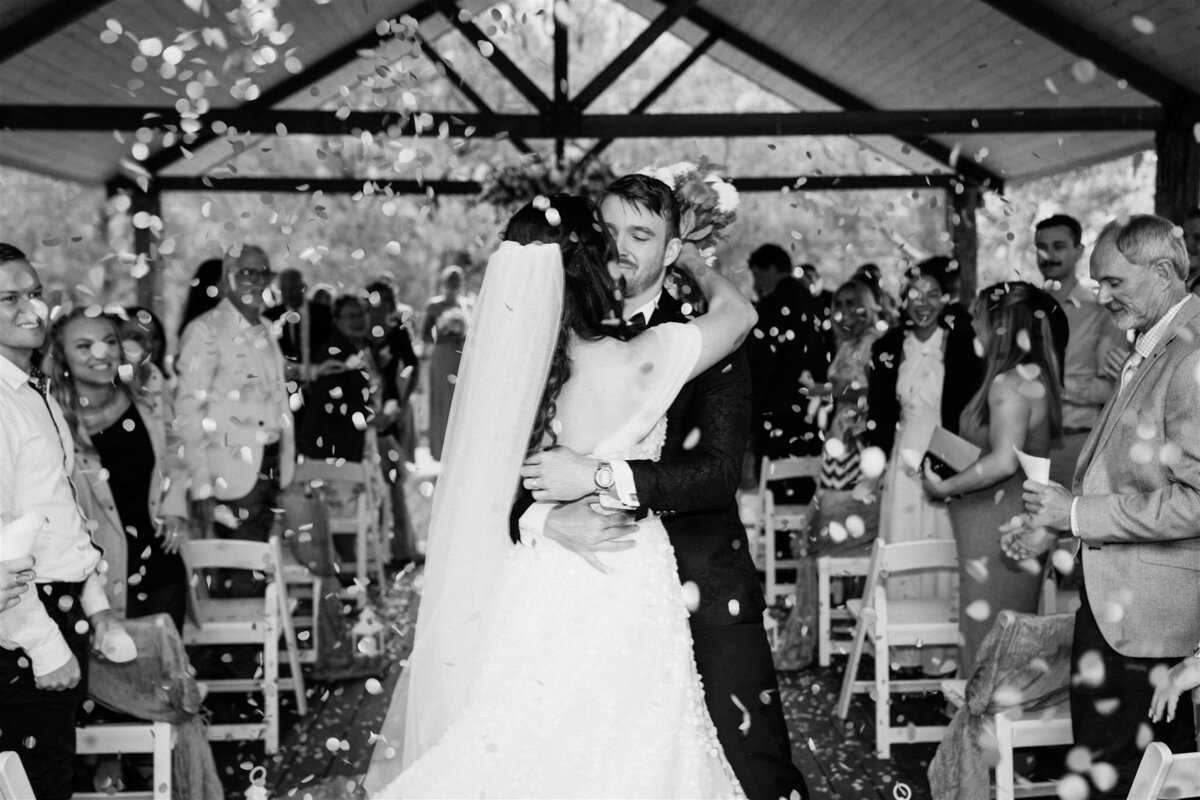 A newly married couple, beaming with joy and intertwined, gracefully exit the ceremony, their love captured in a candid moment.