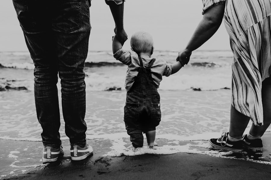föräldrar håller litet barn i handen som känner på vattnet vid havet i halmstad