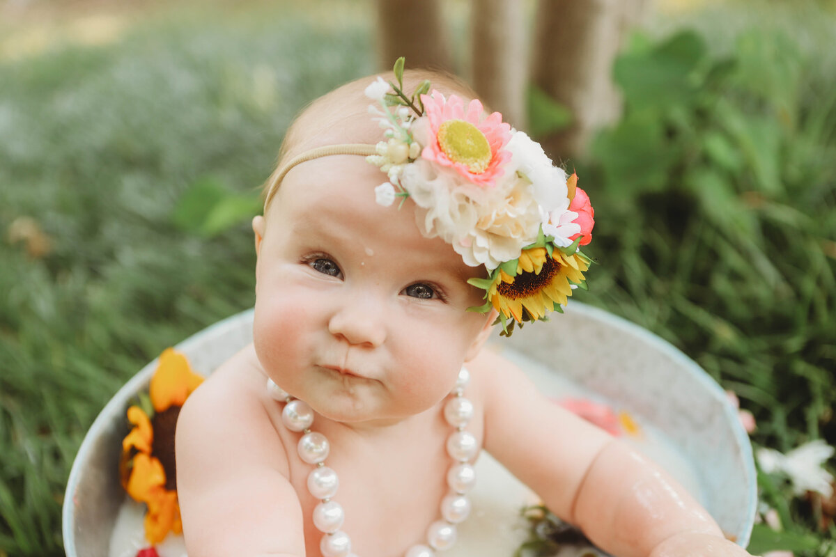 child with flower headband sitting in milk bath